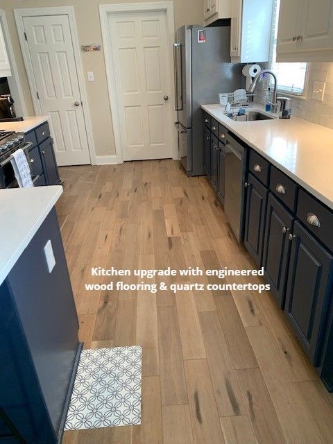 Kitchen with engineered wood flooring, navy cabinets, quartz countertops, and a white door.