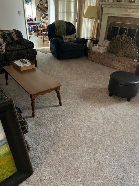 Living room with light-colored carpet, furniture, fireplace, and open doorway to dining area.