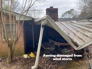 Damaged awning on a brick house after a wind storm. The roof is partially collapsed with debris.