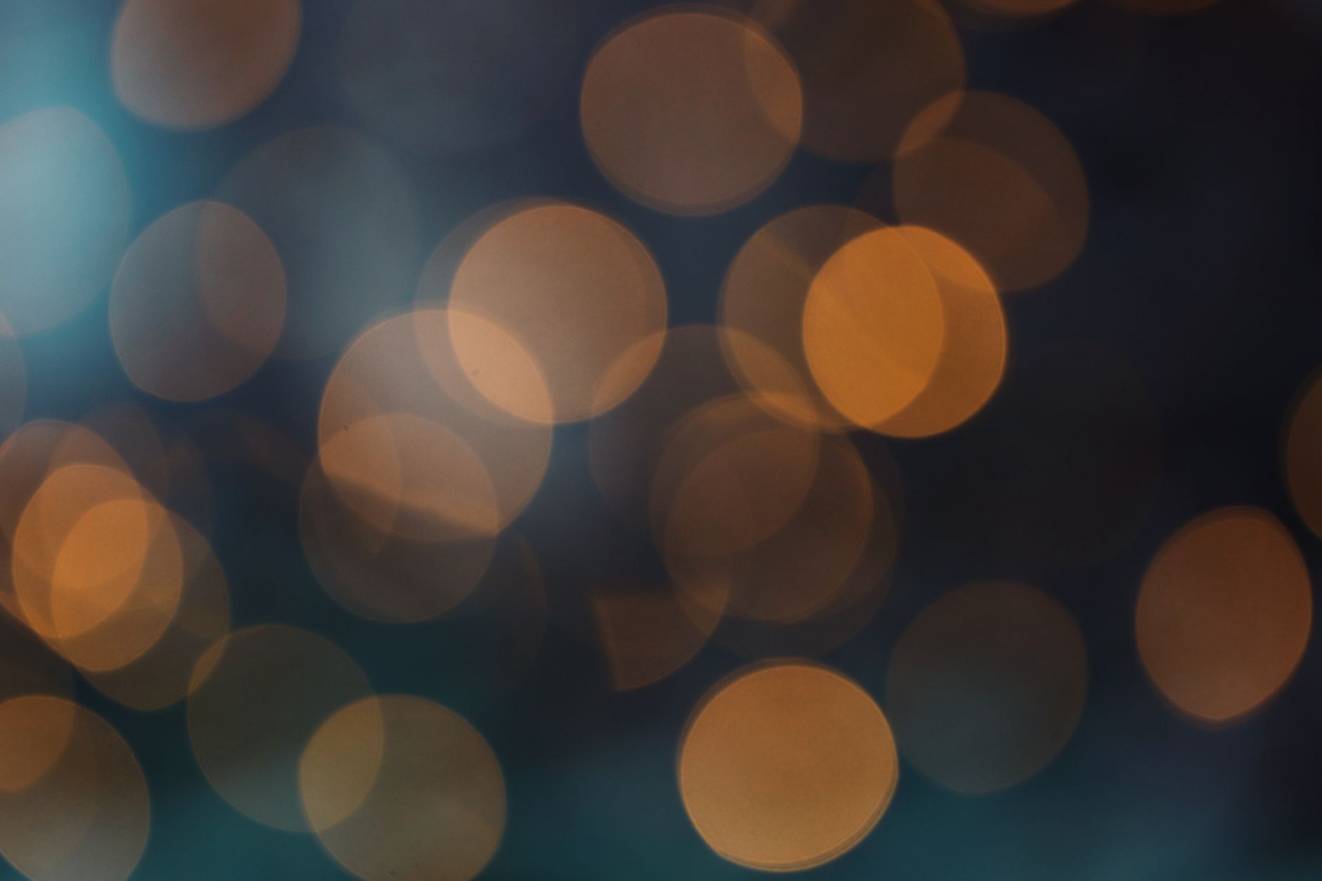 An abstract close-up of blurred warm amber and cool teal bokeh light circles glowing against a dark background, with no literal subject visible.