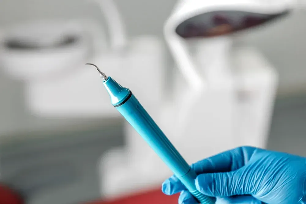 Gloved hand holding a blue dental scaler in a clinic setting