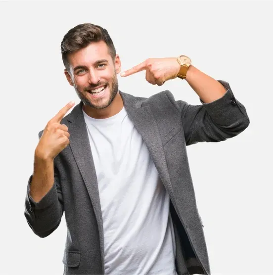 Smiling man in gray blazer and white shirt pointing at his face against a white background