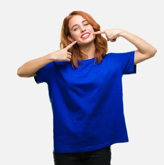 Smiling person in a blue shirt pointing to their cheeks against a white background