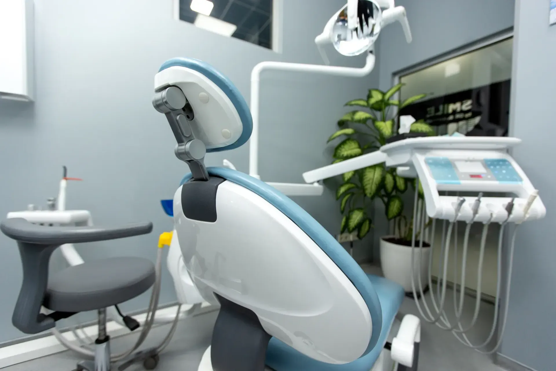 Modern dental clinic with a patient chair, overhead light, and equipment beside a sink and plant.