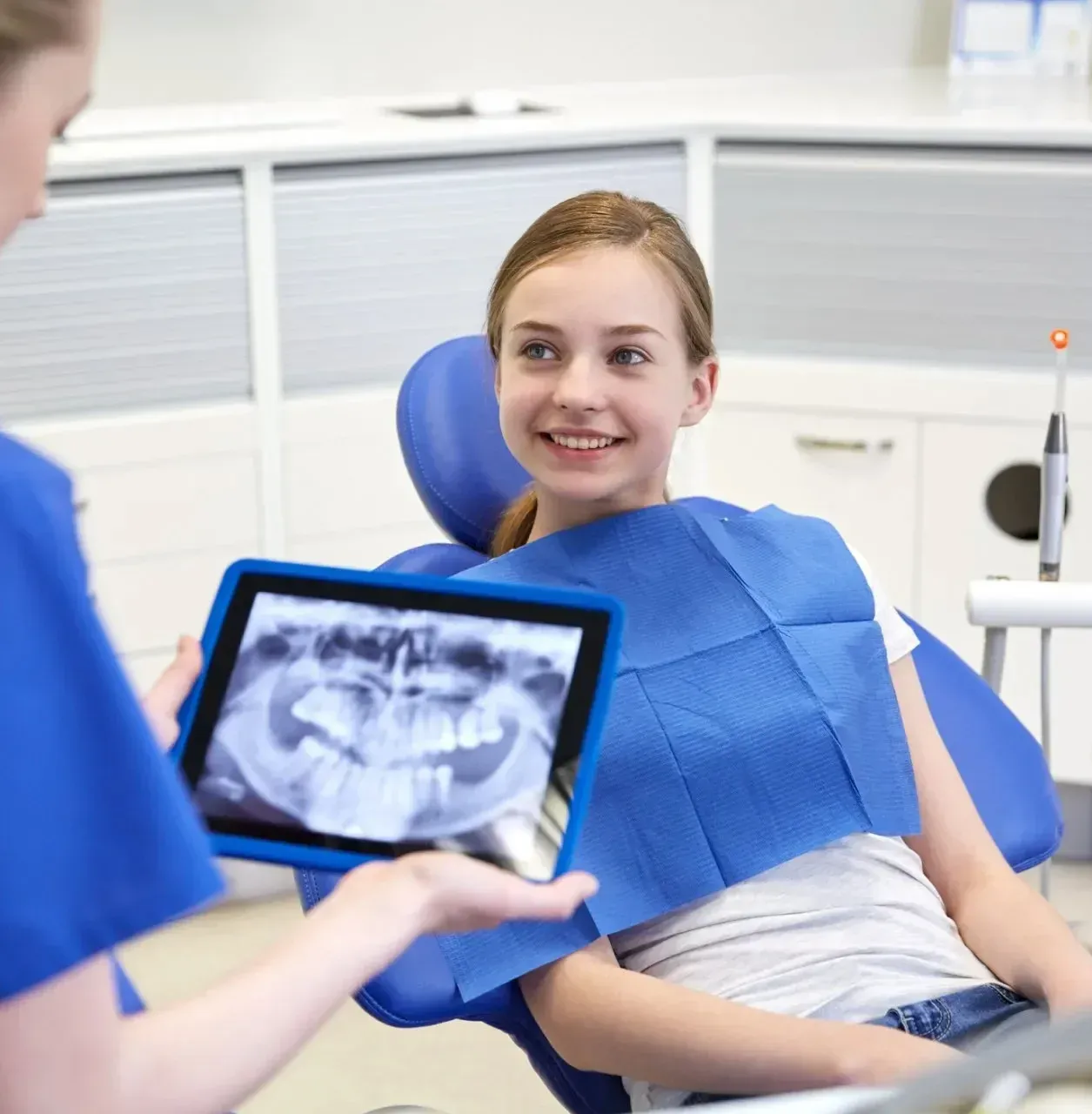 Dental patient smiling in a chair while a dentist shows an X-ray on a tablet