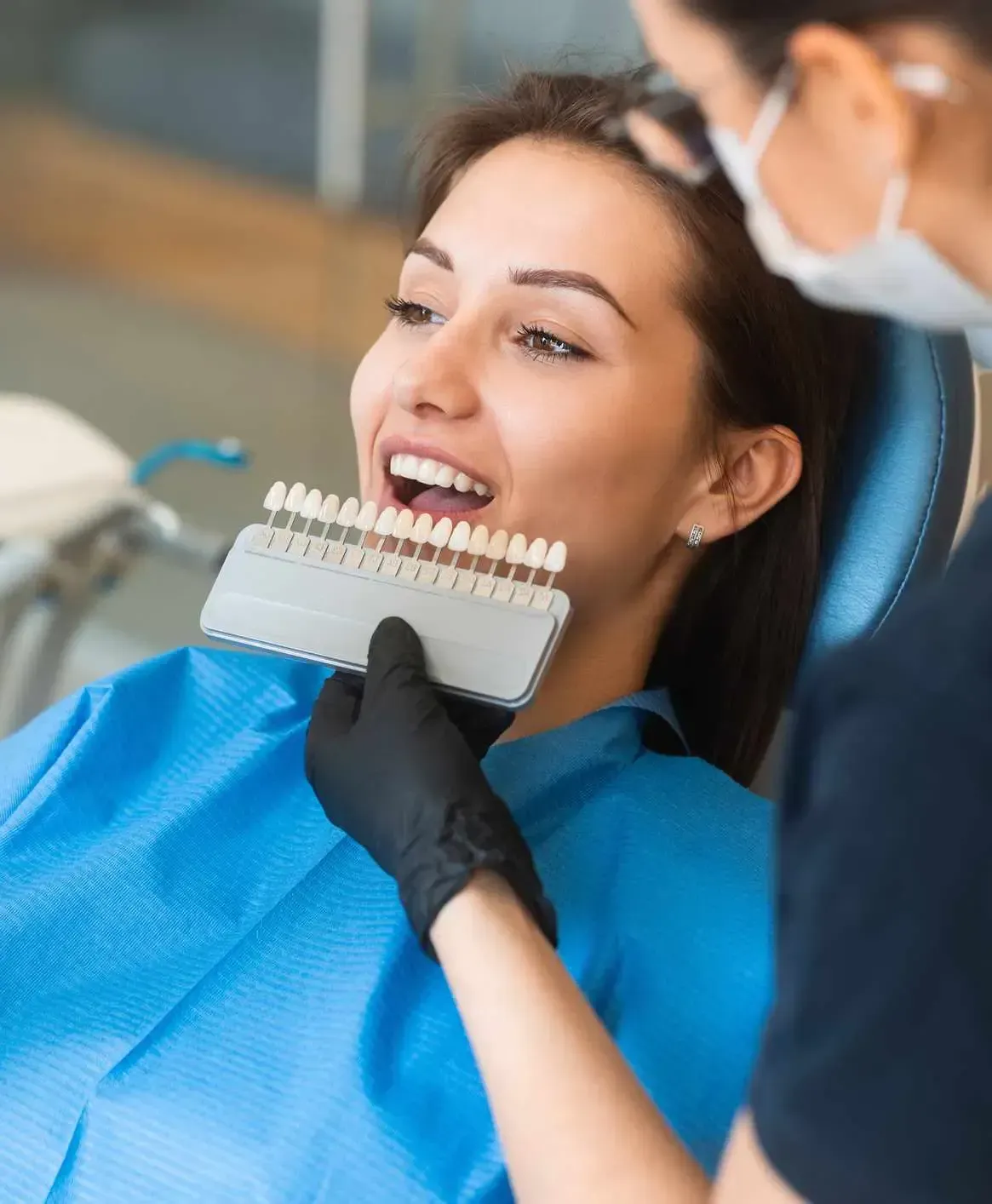 Dentist showing tooth shade guide to a smiling patient in a dental chair