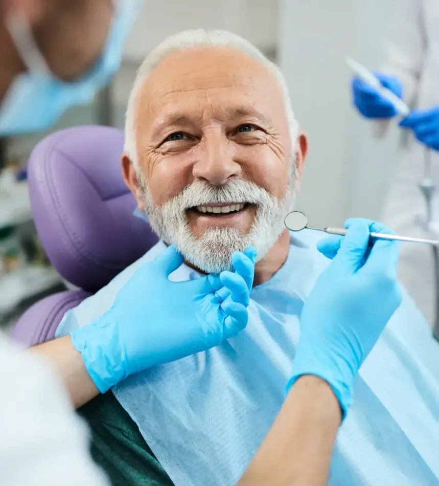 Smiling patient in dental chair as dentist examines teeth with gloved hands