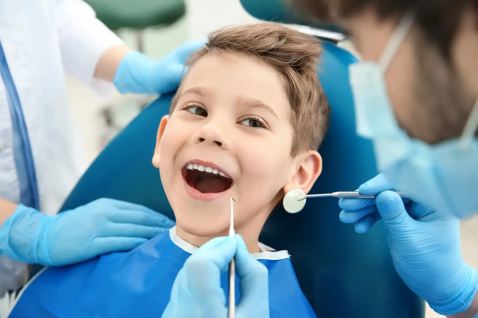 Child at the dentist, smiling during a dental exam with blue gloves and tools.