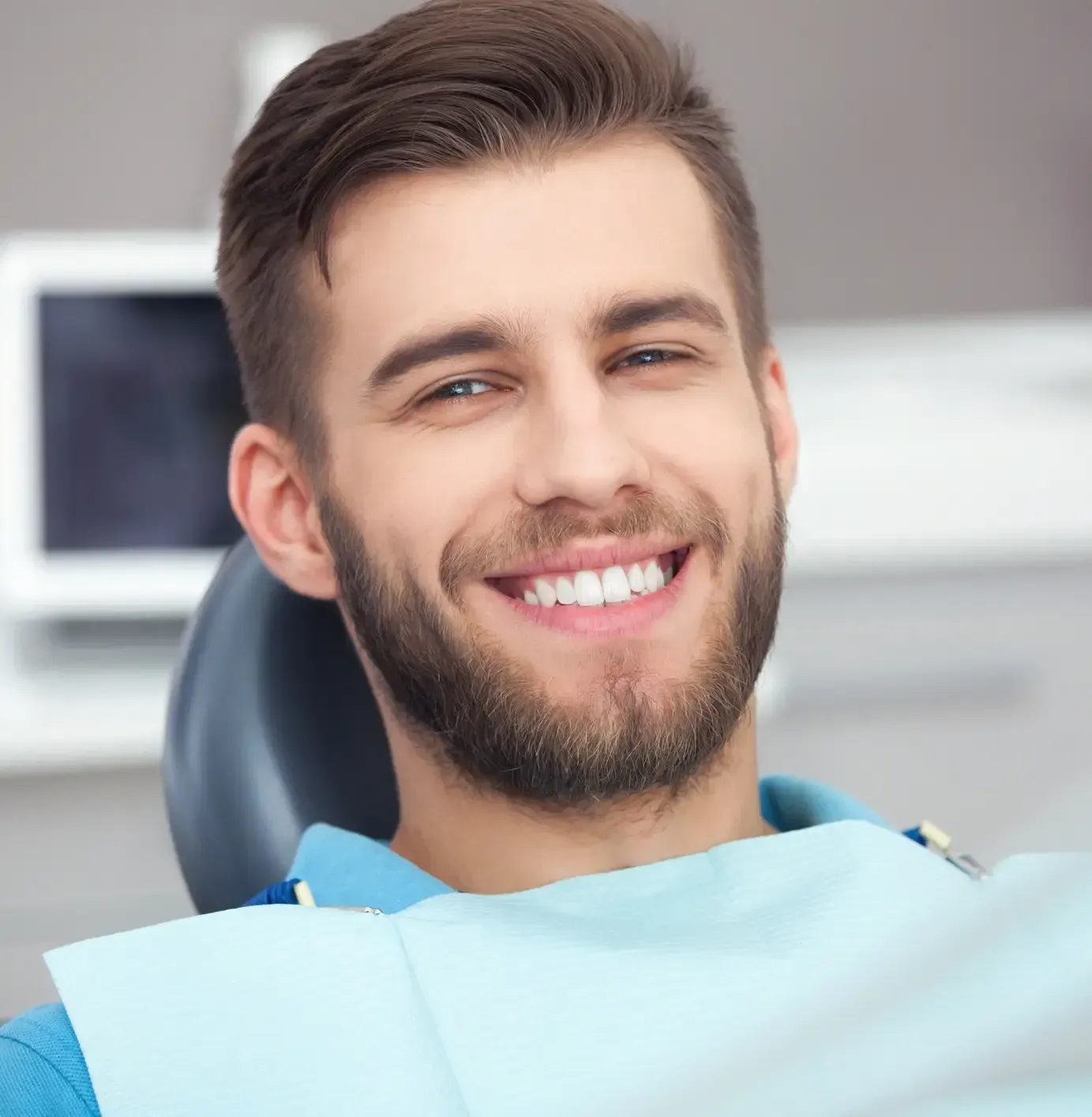Smiling dental patient in a chair with a blue bib in a bright clinic
