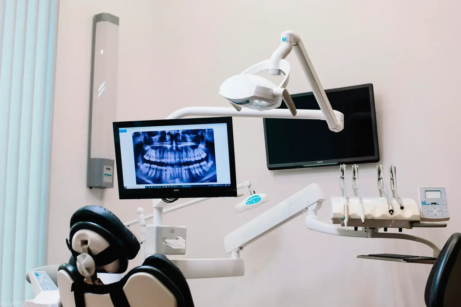 Dental exam room with chair, monitors, and overhead light displaying an X-ray.
