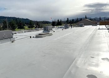 The roof of a building with a white roof and trees in the background.