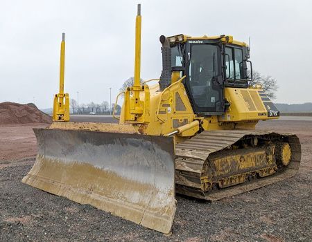 Yellow bulldozer with a large front blade on a dirt lot under an overcast sky