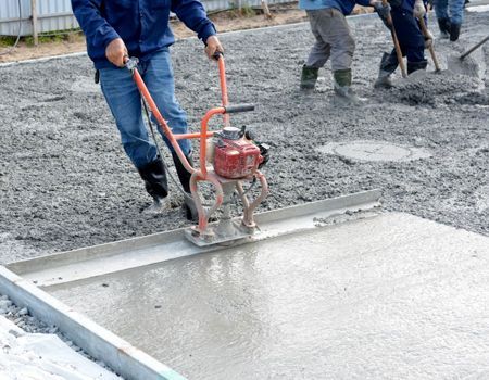 Workers using a power screed to level wet concrete on a construction site