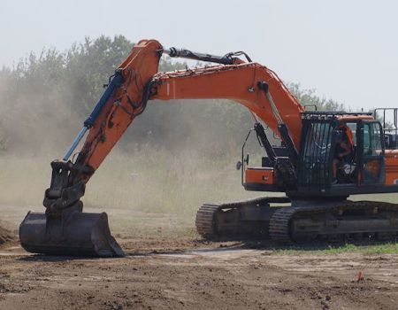 Orange excavator digging in a dusty construction site with a raised bucket
