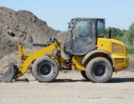 Yellow front-end loader at a gravel site, parked beside a large dirt pile under a clear sky