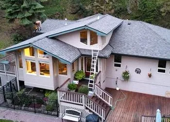 A house with gray shingled roofs and a tall ladder extending from a deck to the roof.