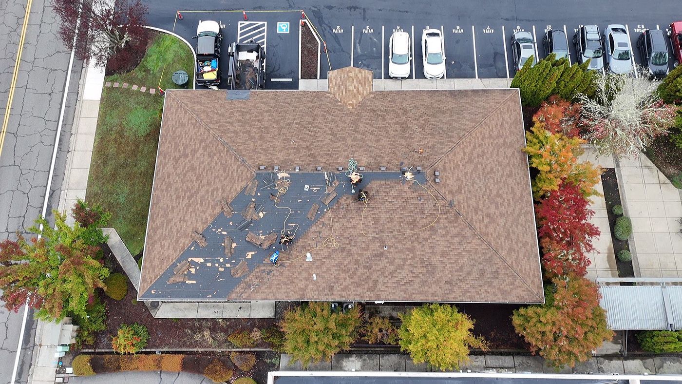 Aerial view of a brown-roofed building with workers; surrounded by trees, parking lot, and cars.