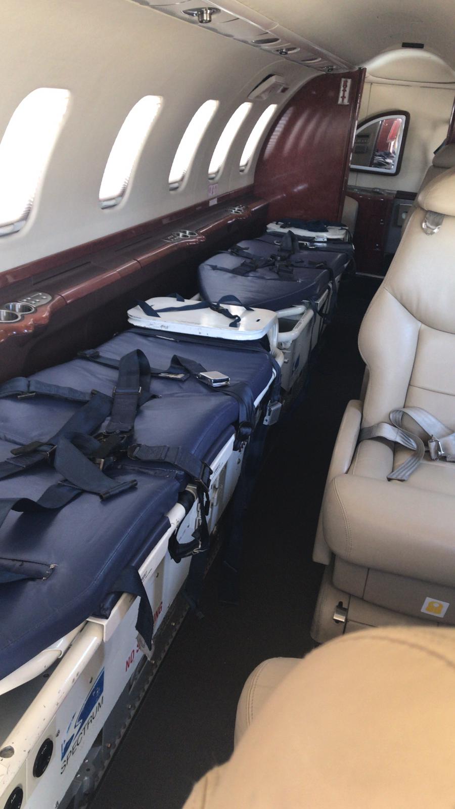 Dentro de una ambulancia aérea: camillas aseguradas a lo largo, asientos beige a la derecha, vistas desde las ventanas.