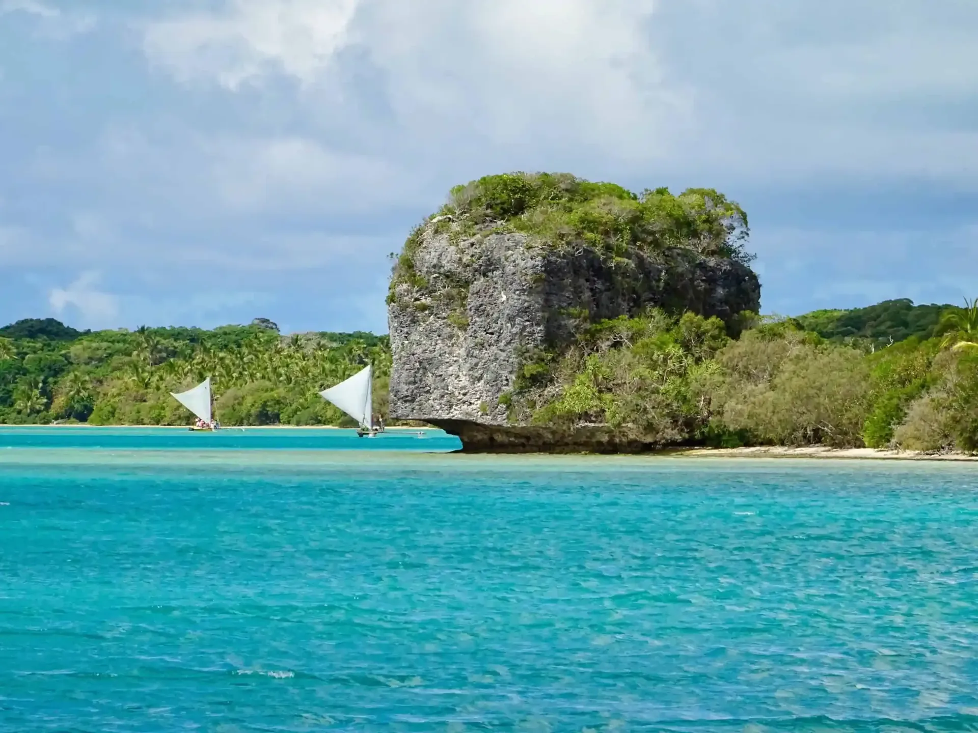 A large rock in the middle of a body of water with two sailboats in the water.