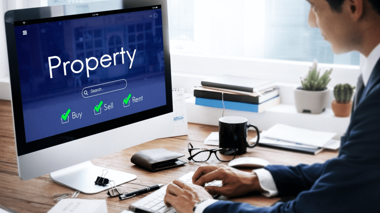 A man is sitting at a desk in front of a computer with the word property on the screen.