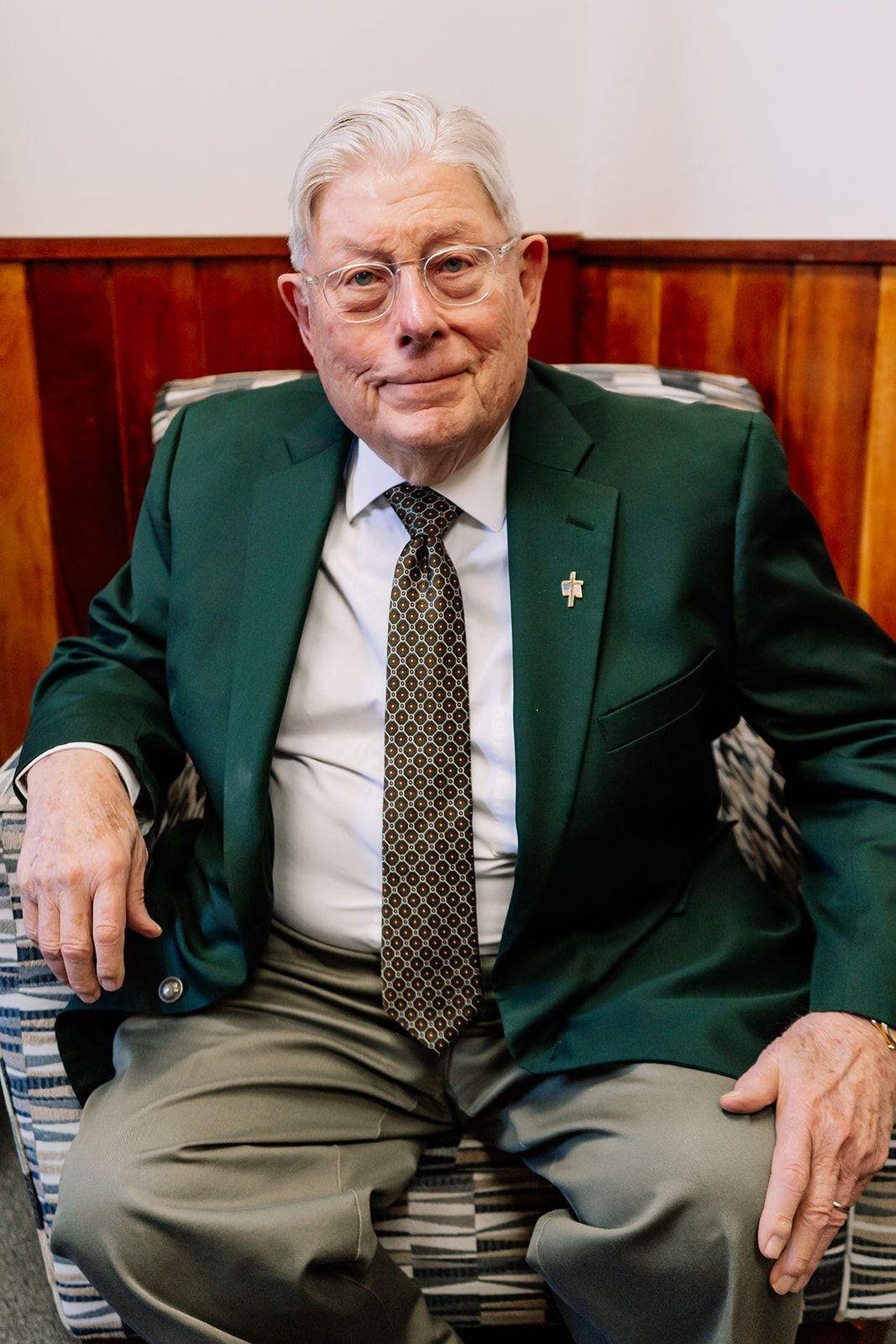 A man in a green jacket and tie is sitting in a chair.