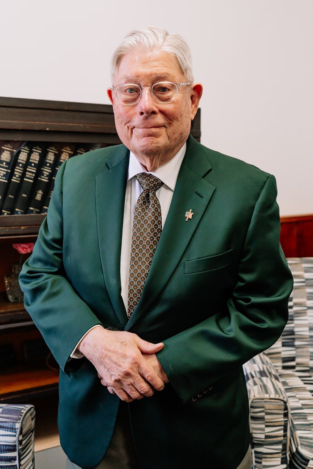 A man in a green suit and tie is standing in front of a stack of books.