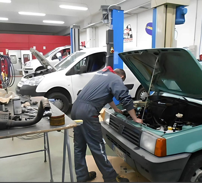 Un meccanico lavora su un'auto verde in un'officina, con altri veicoli sui ponti sollevatori nelle vicinanze.