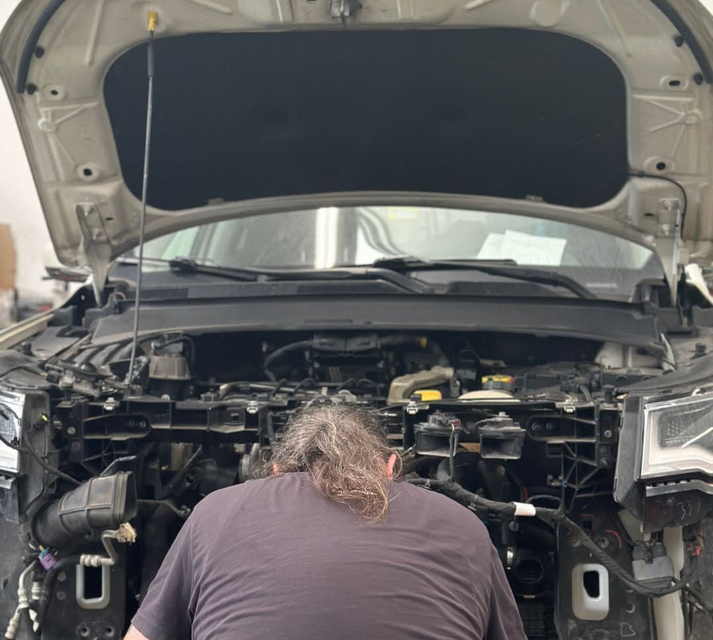 Meccanico al lavoro sotto il cofano aperto di un'auto in un'officina.