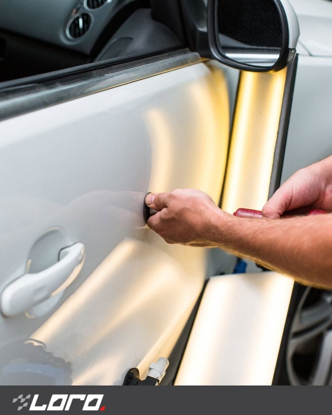 Persona che utilizza un prodotto giallo per rimuovere le ammaccature dalle portiere di un'auto su una portiera argentata.