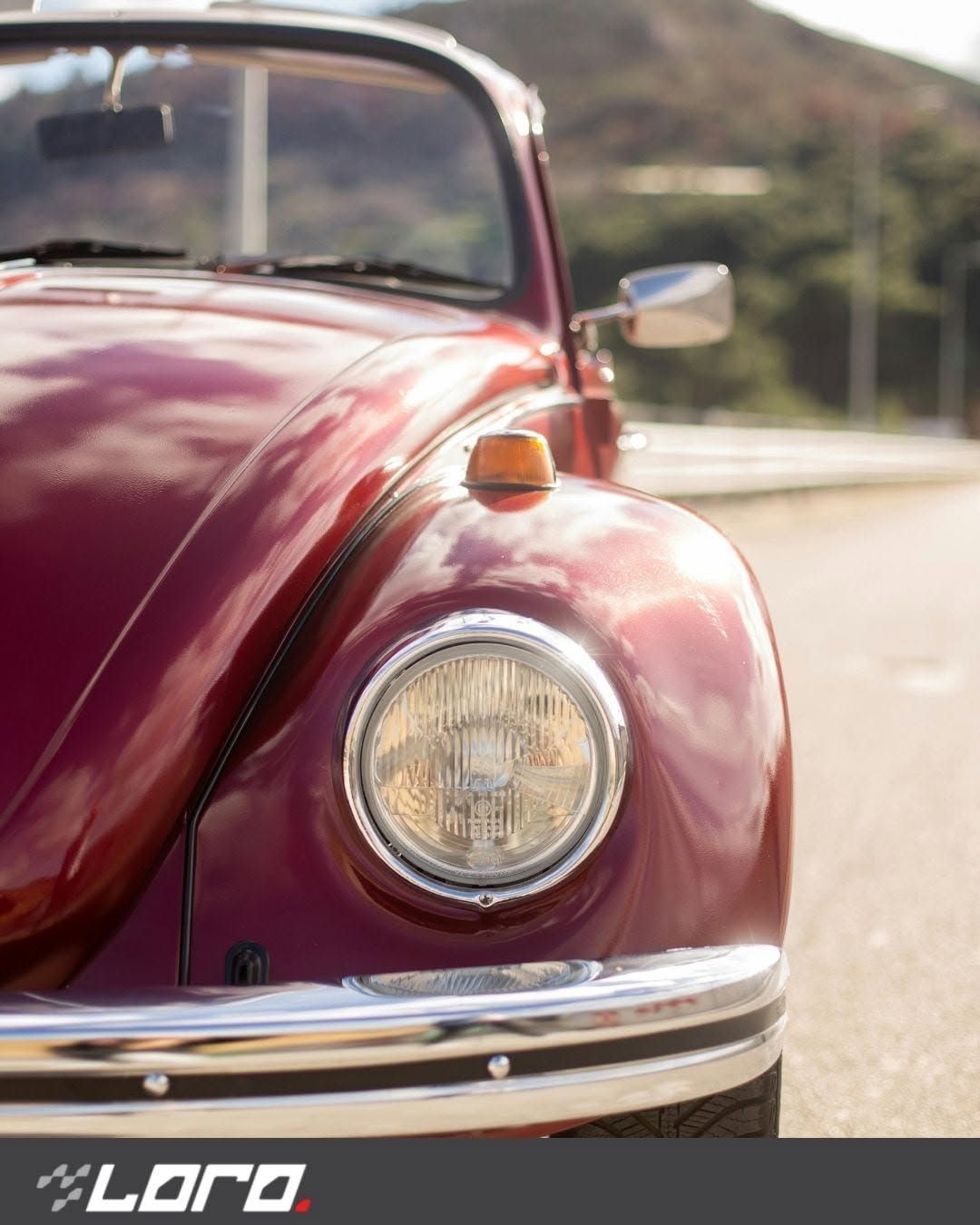 Primo piano di un Maggiolino Volkswagen d'epoca rosso parcheggiato su una strada soleggiata.