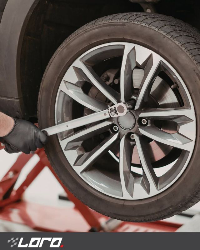 Mano guantata che stringe un dado di fissaggio su una ruota di un'auto con una chiave inglese su un ponte sollevatore