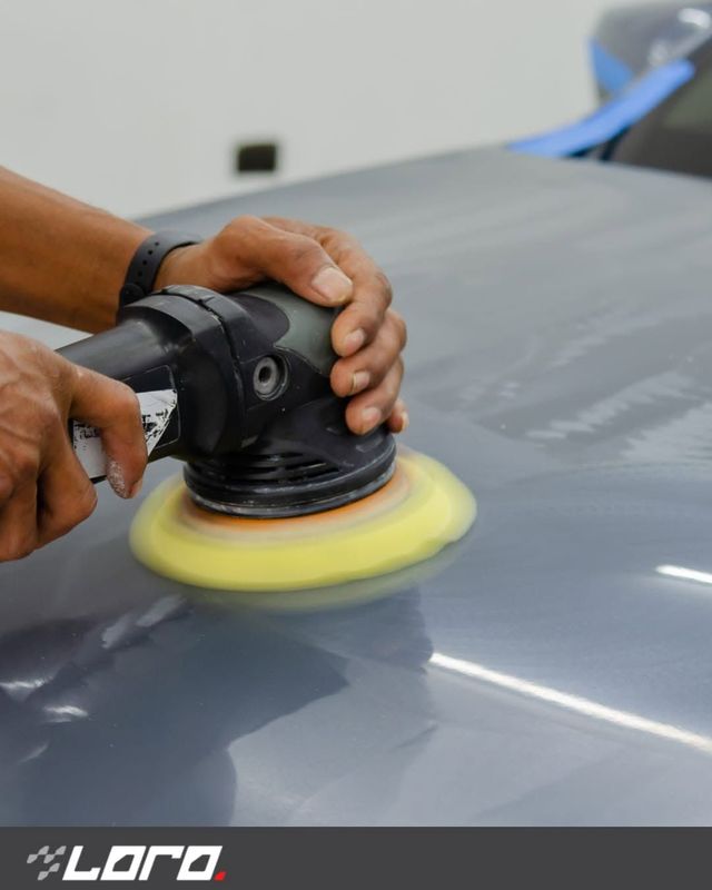 Mani che utilizzano una lucidatrice elettrica per lucidare la superficie grigia di un'auto con un tampone giallo.