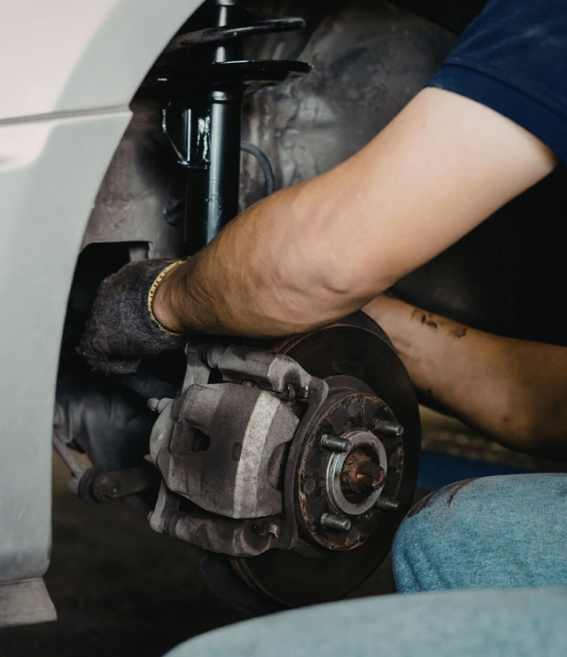 Un meccanico sostituisce il disco e la pinza del freno di un'auto utilizzando un cric all'interno del passaruota.