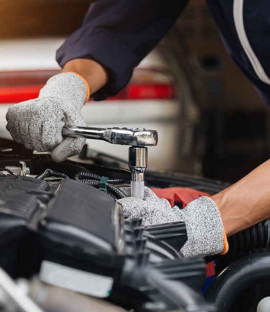 Mani guantate che usano una chiave a cricchetto per riparare il motore di un'auto in un'officina.