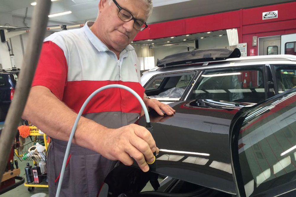 Un meccanico, con indosso una camicia rossa e grigia, lucida un'auto nera in un'officina.