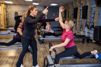 Person balancing on a reformer Pilates machine in a gym studio with wall posters in the background