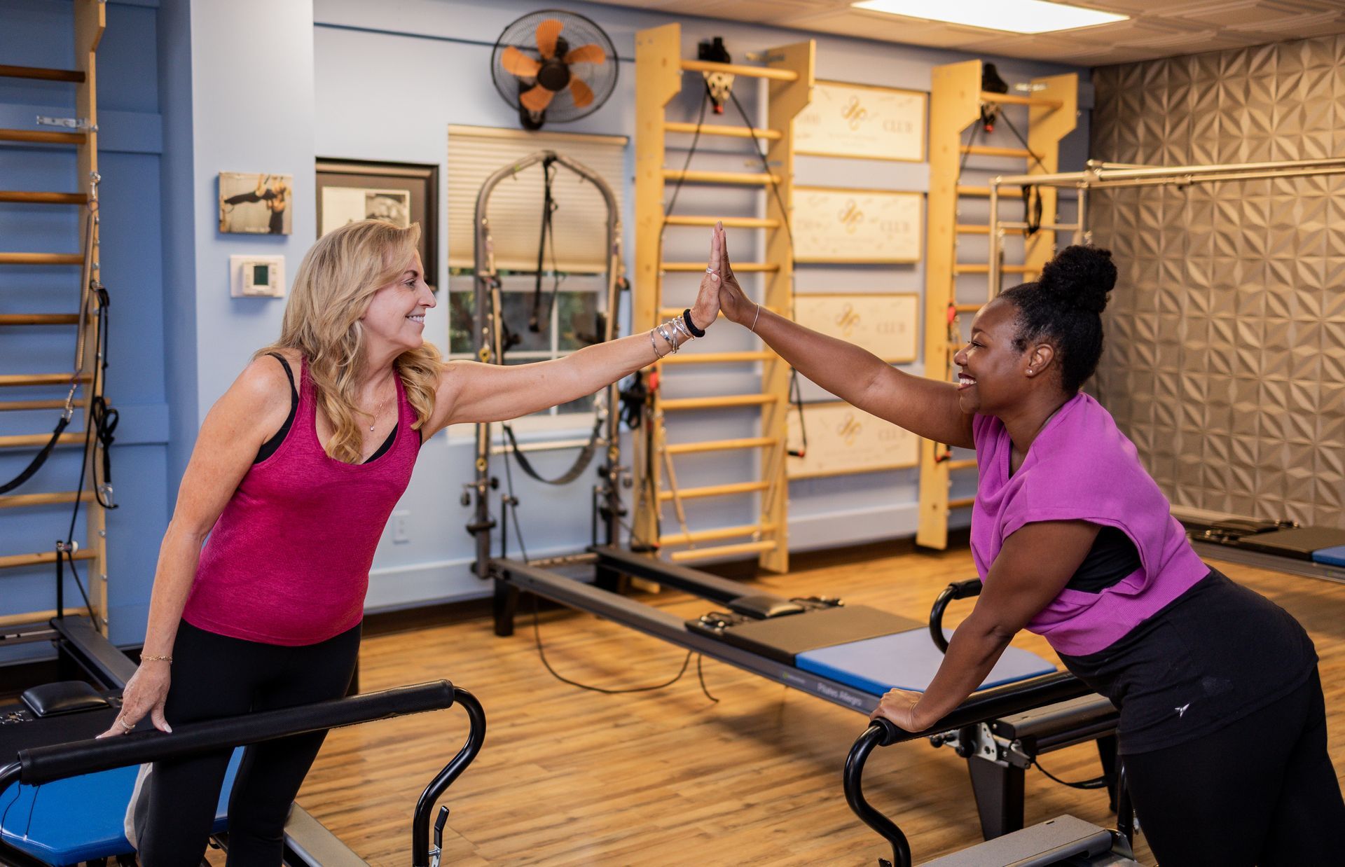 Woman stretching on a Pilates reformer machine in a studio, wearing blue striped leggings.