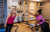 Woman stretching on a Pilates reformer machine in a studio, wearing blue striped leggings.