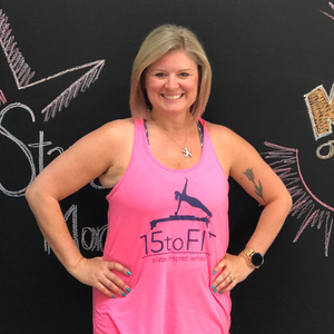 Smiling woman in pink tank top standing with hands on hips before a chalkboard wall.