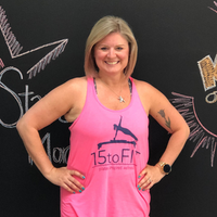 Smiling woman in pink tank top standing with hands on hips before a chalkboard wall.