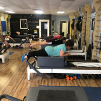 People exercising on pilates reformers in a studio with wooden floors and mirrors
