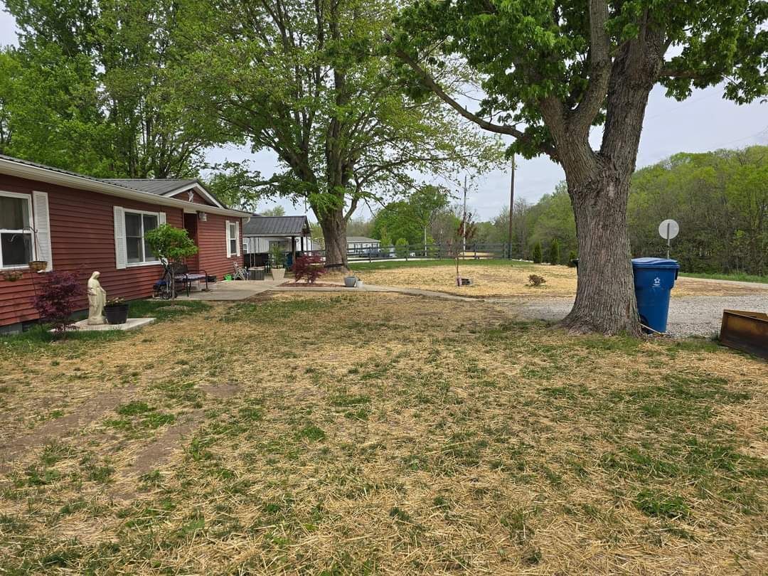 A grassy front yard with a brown house and large trees on a cloudy day.