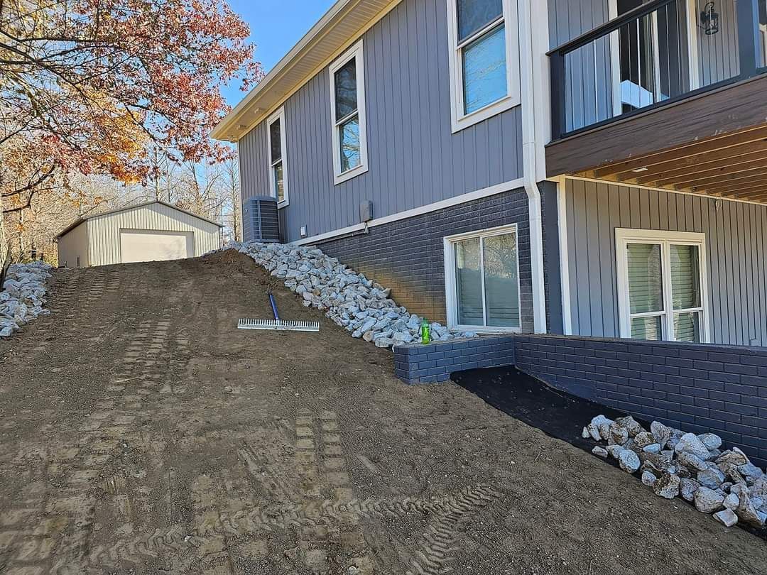 Exterior view of a house with a steep slope of dirt, rocks, and a shed.