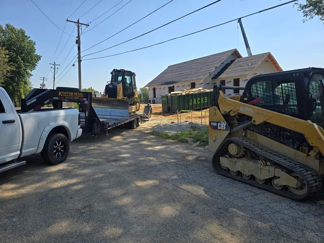 Construction site with truck, trailer, bulldozer, skid steer, and partially built building.