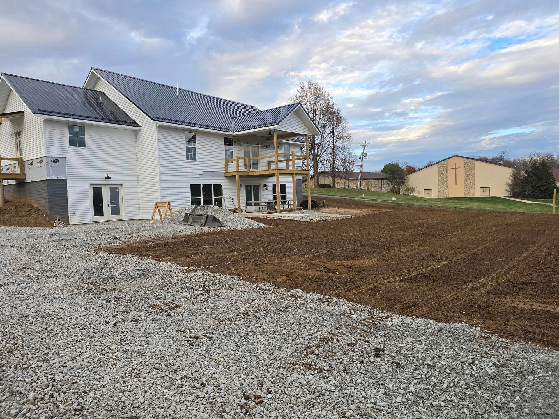 House under construction with gravel and dirt in foreground. Cloudy sky.
