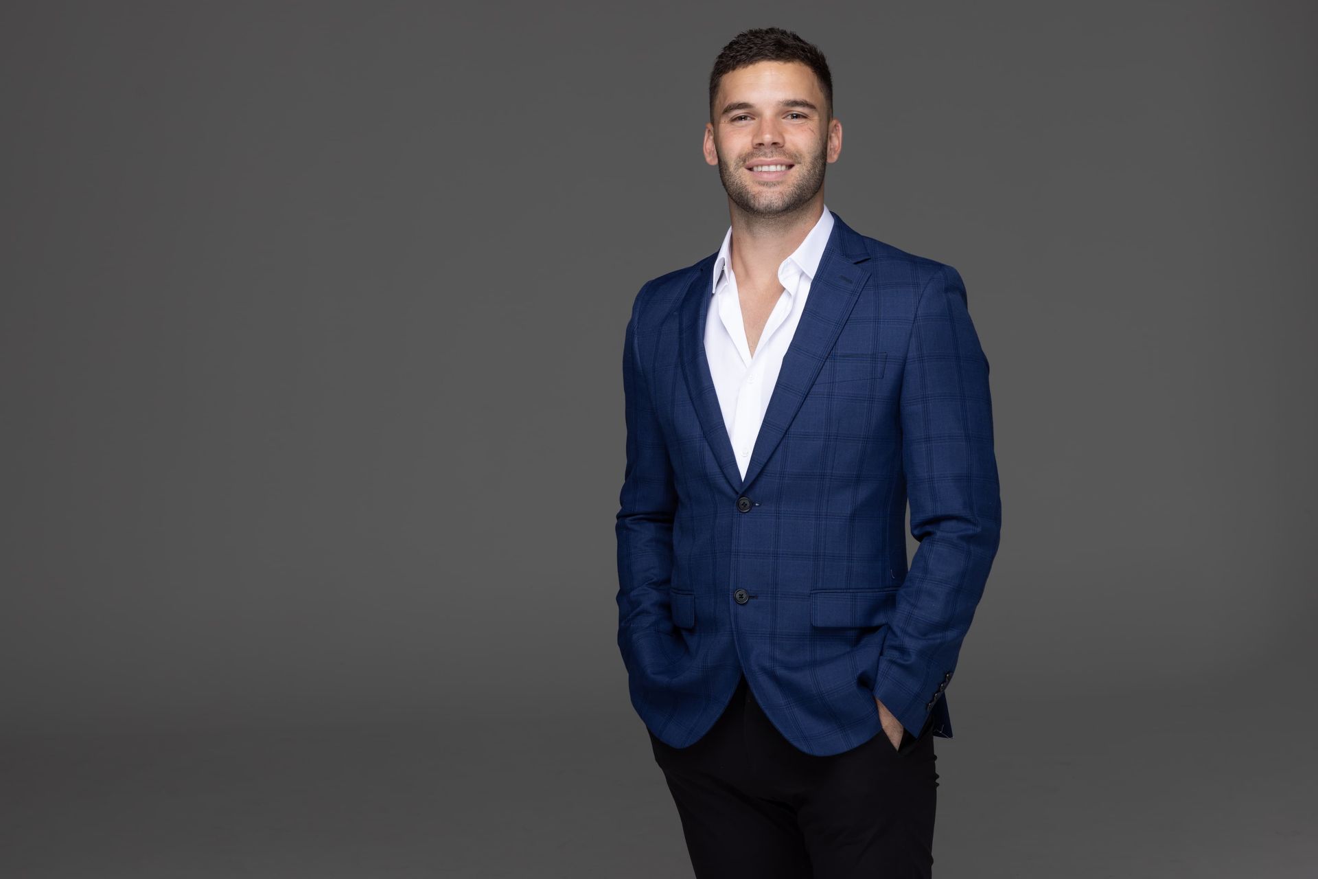 Tyler Cornish in a blue suit and white shirt stands with his hands in his pockets