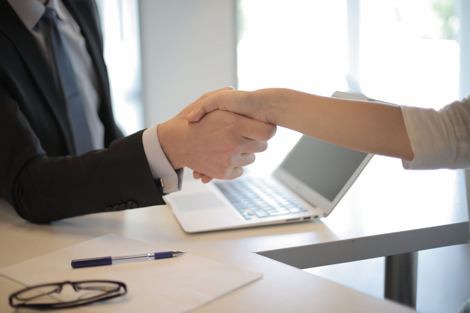 a mortgage broker and a woman are shaking hands while sitting at a table with a laptop
