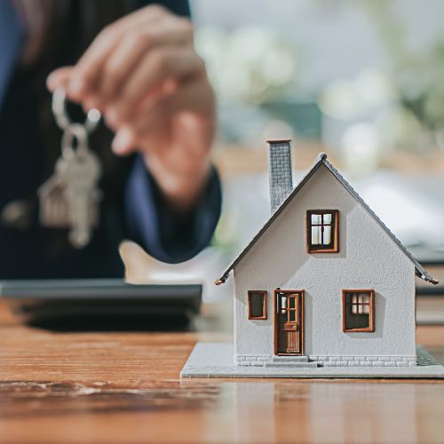 A woman is holding a key next to a model house on a table.