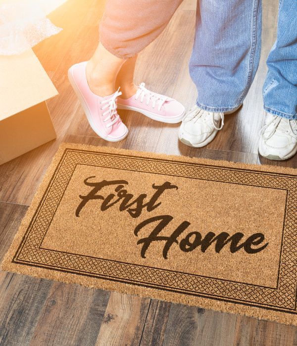 a couple standing on a door mat that says first home - first home loan gold coast