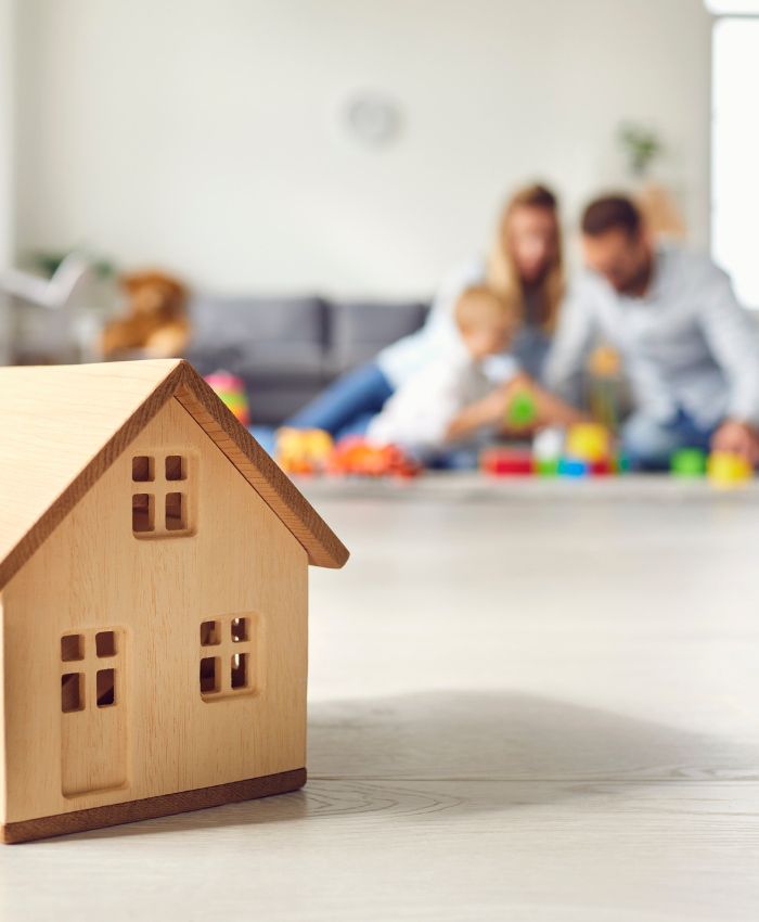 a family is playing with toys on the floor with a small wooden house in the foreground - refinancing gold coast